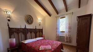 A bedroom with a large bed, wooden headboard, two wall sconces, a window with curtains, and a door. - Apartment on wooded land 2 minutes from the beaches and the center (Propriano)