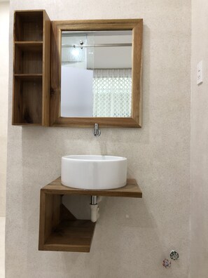 A bathroom with a wooden medicine cabinet, a white sink, and a mirror. - Yellow House Boutique (Nha Trang)