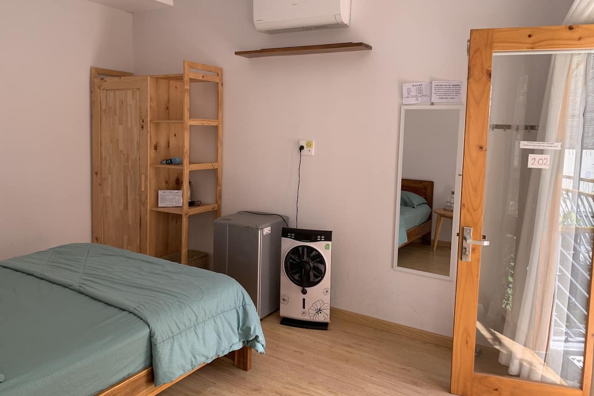 A bedroom with a bed, a washing machine, a wooden wardrobe, an air conditioner, and a door with a sign.
