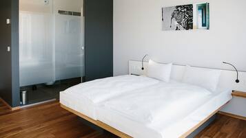 A modern bedroom with a large bed, a glass shower enclosure, and a minimalist design.
