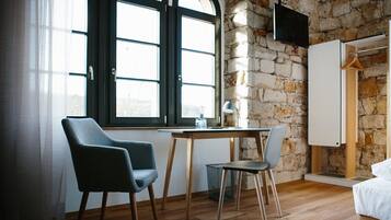 Ein Zimmer mit Steinwand, einem Bett, einem Schreibtisch mit Stuhl und einem Fenster mit Vorhängen.