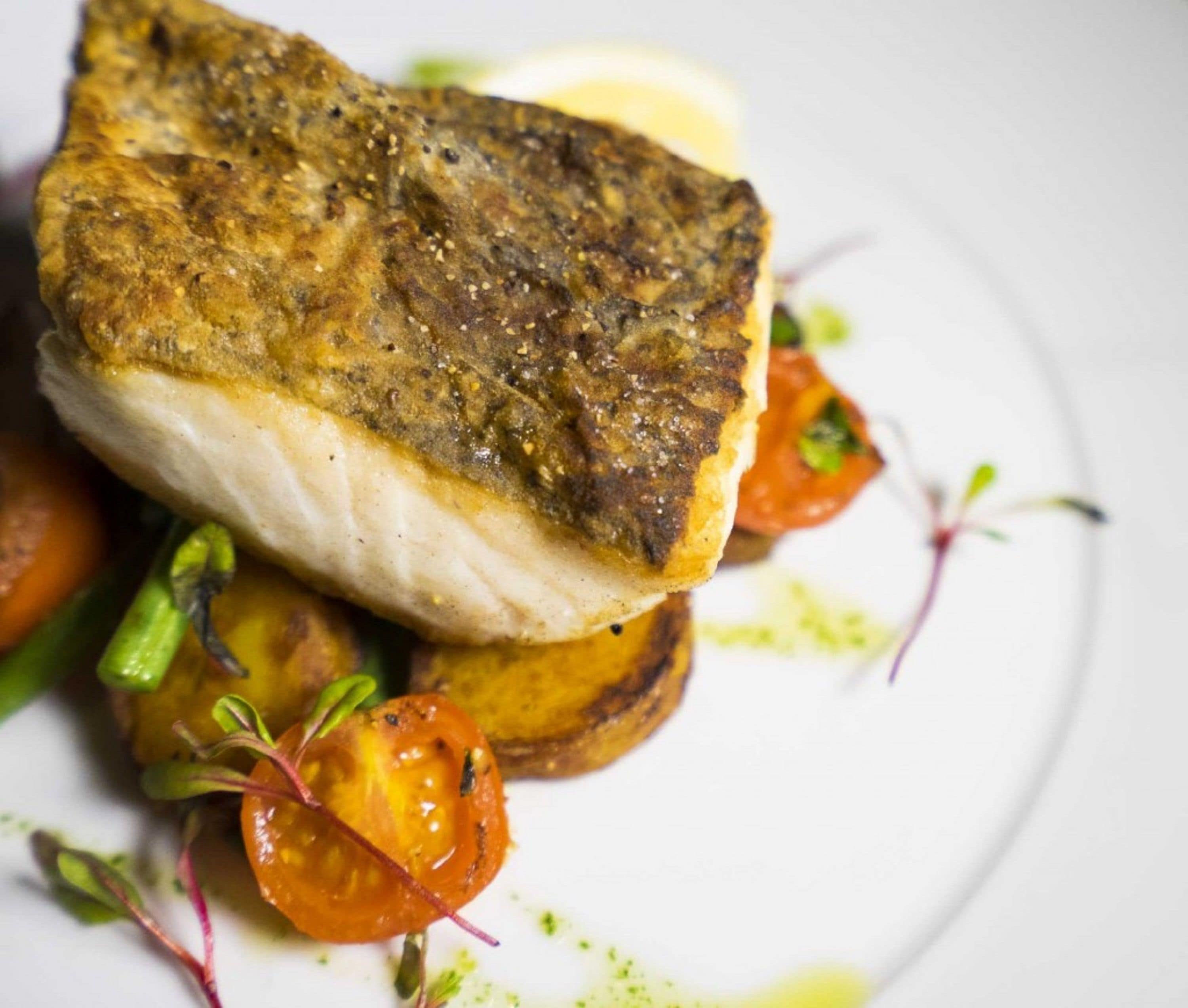 Ein Teller mit Fisch, Bratkartoffeln und Kirschtomaten.