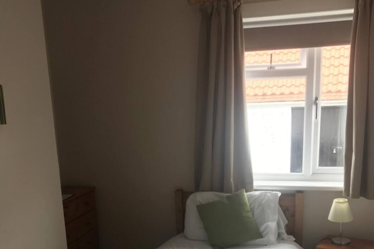 Un llit ben fet amb una tovallola doblegada, una làmpada de nit i una finestra amb cortines.