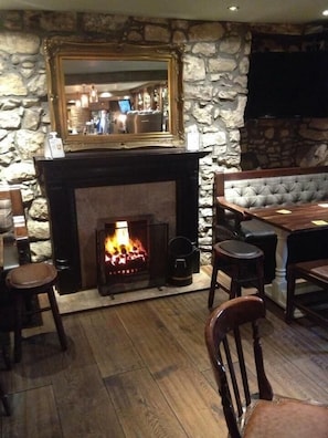 A stone-walled room with a fireplace, a mirror above it, and a seating area with a table and chairs. - Riccarton Inn (Edinburgh)