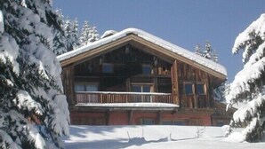 A log cabin with a balcony, surrounded by snow-covered trees.