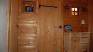 A wooden cabin interior with a large door, a small window, and a dresser with drawers.