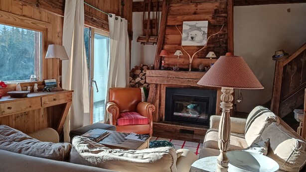 A cozy cabin interior with a fireplace, wooden walls, a leather armchair, and a dining table.