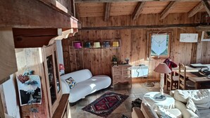 A cozy wooden cabin interior with a white sofa, a dining table, and a rug.