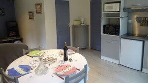 A compact kitchen with a microwave, toaster, and refrigerator. A dining table with plates and a wine bottle is set in the center. - In a stunning location with a beautiful ocean view; the beach is just 1 minute away (Pénestin)