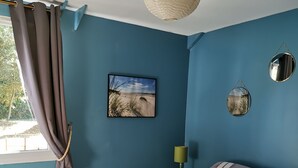 A bedroom with a bed, a window with curtains, a wall-mounted lamp, and a beach picture. - In a stunning location with a beautiful ocean view; the beach is just 1 minute away (Pénestin)