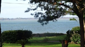 A view of a grassy area with a tree and a bird feeder, leading to a body of water. - In a stunning location with a beautiful ocean view; the beach is just 1 minute away (Pénestin)