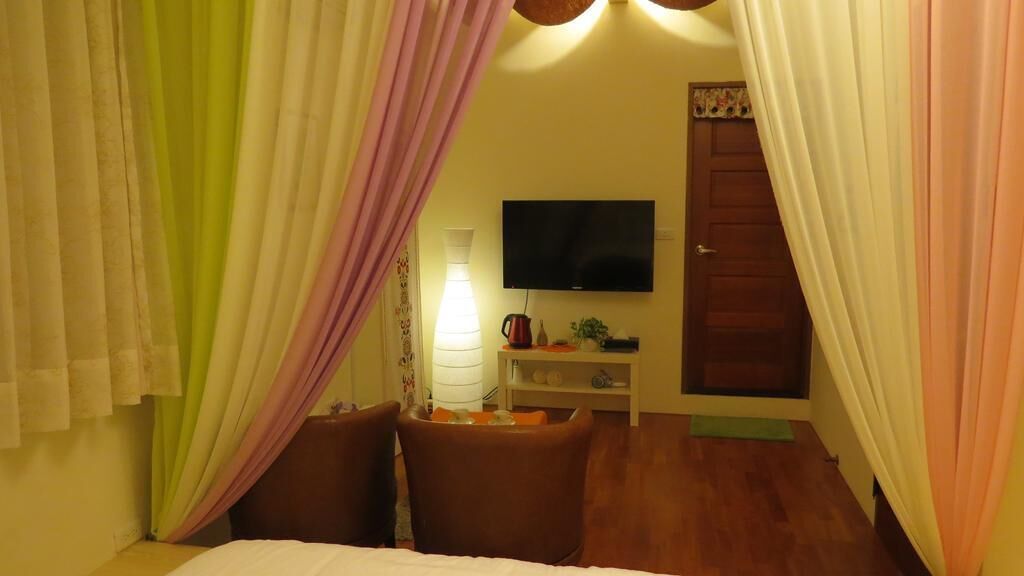 Um quarto com uma cama, duas cadeiras, uma televisão, um abajur e uma porta.