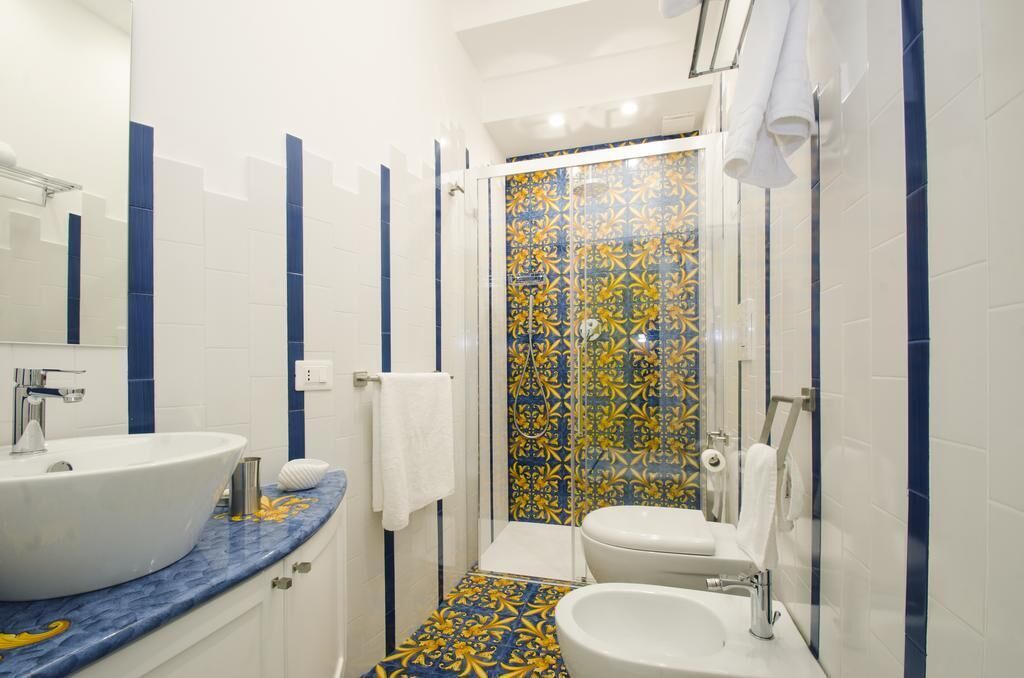 A bathroom with a white sink, a white toilet, and a shower with a patterned tile wall.