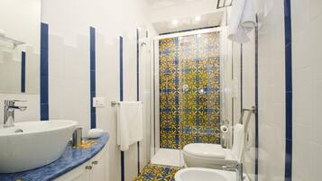 A bathroom with a white sink, a white toilet, and a shower with a patterned tile wall.
