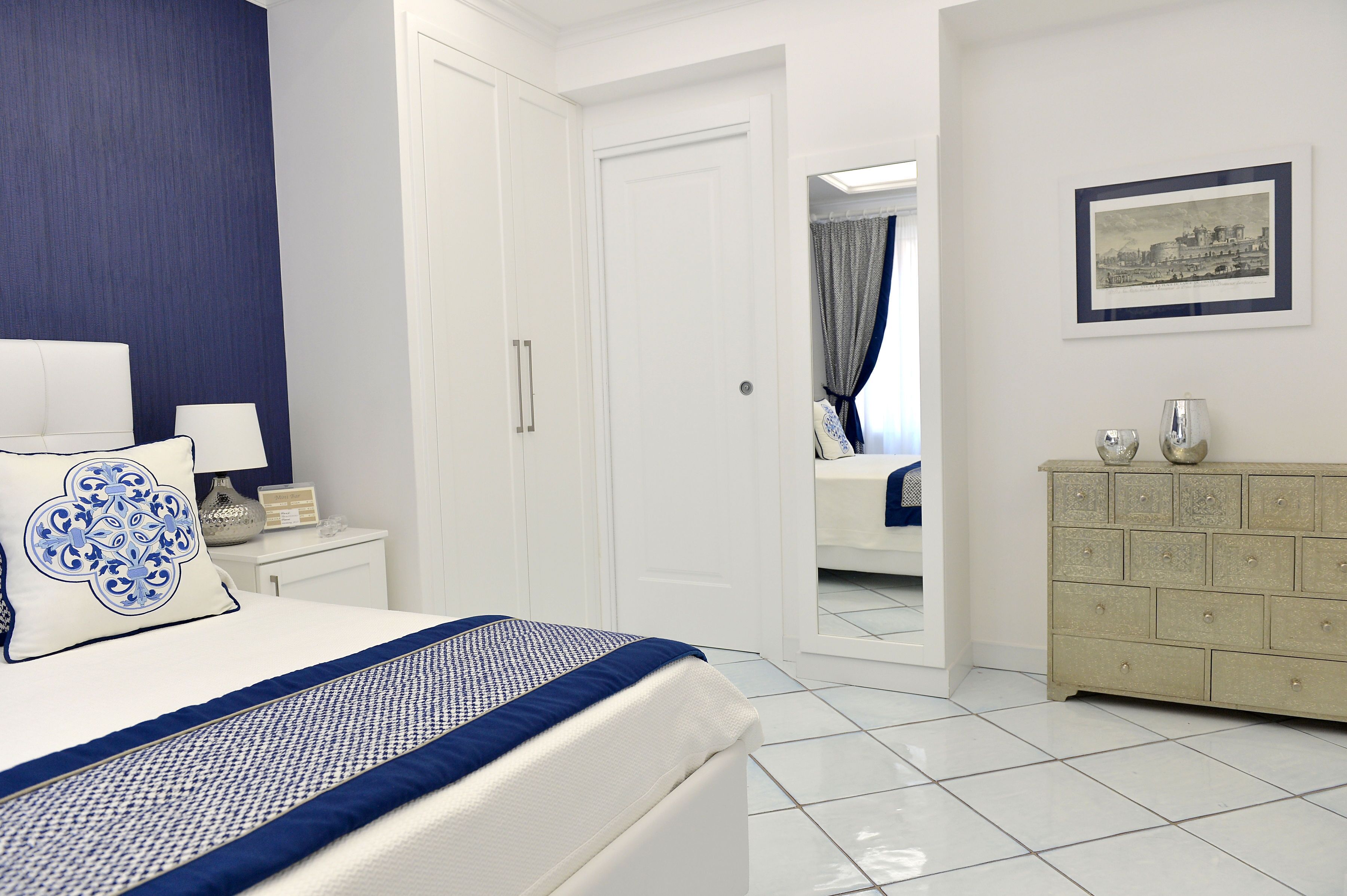 A hotel room with a bed, a nightstand, a dresser, and a framed picture on the wall.