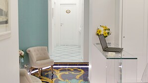 Un pasillo con piso estampado, una mesa de vidrio con una computadora portátil y una silla.