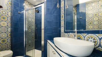 Un baño con un lavamanos grande de color blanco, una cabina de ducha con mampara de vidrio y baldosas azules con diseño.