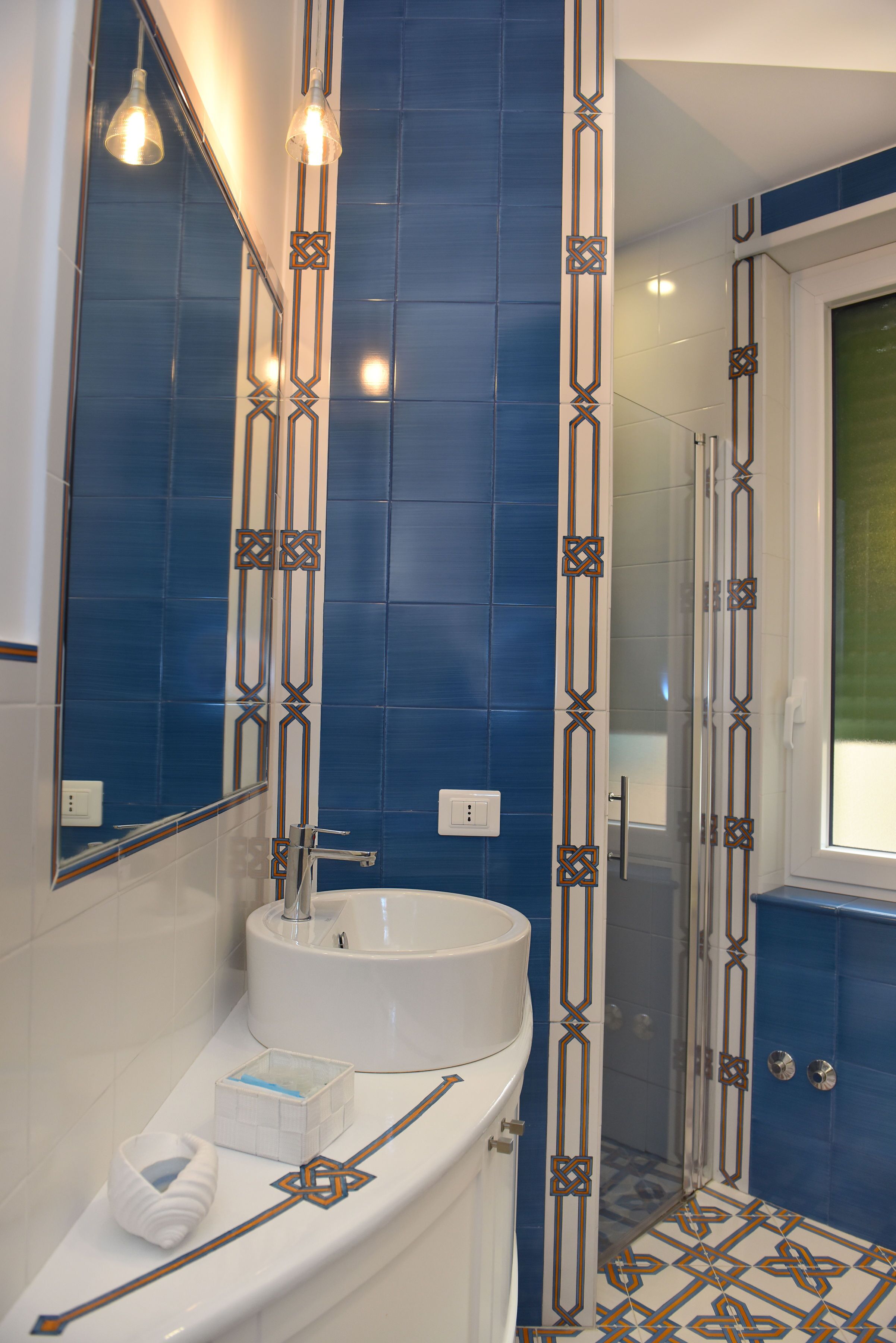 Ein Badezimmer mit einem weißen Waschbecken, blauen Fliesen und einer Duschkabine aus Glas.