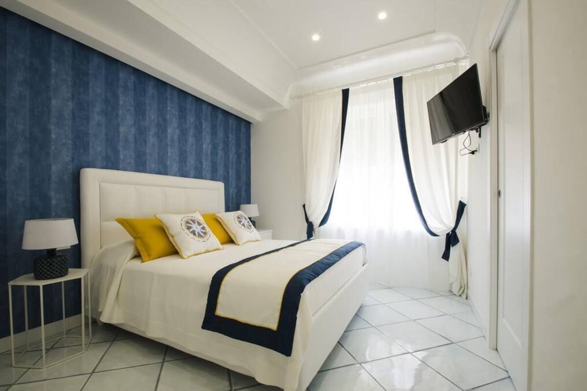Een slaapkamer met een groot bed, nachtkastje, televisie aan de muur en raam met gordijnen.