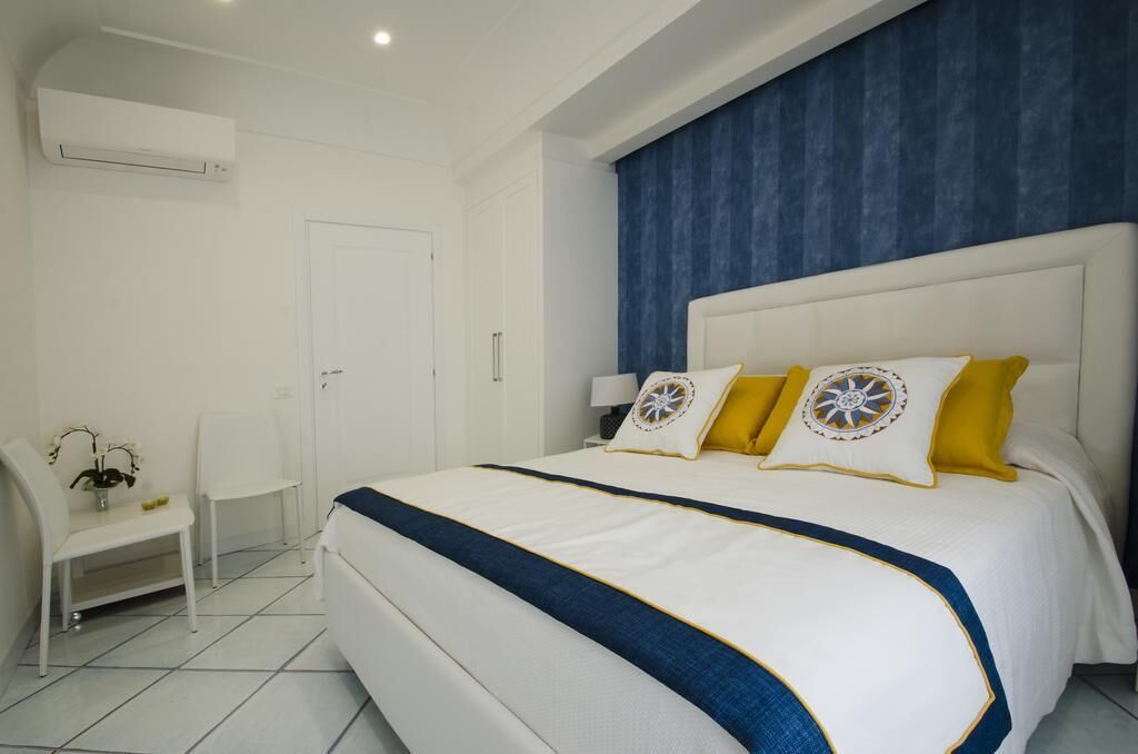 A bedroom with a large bed, white walls, a blue accent wall, and a small white desk with a chair.