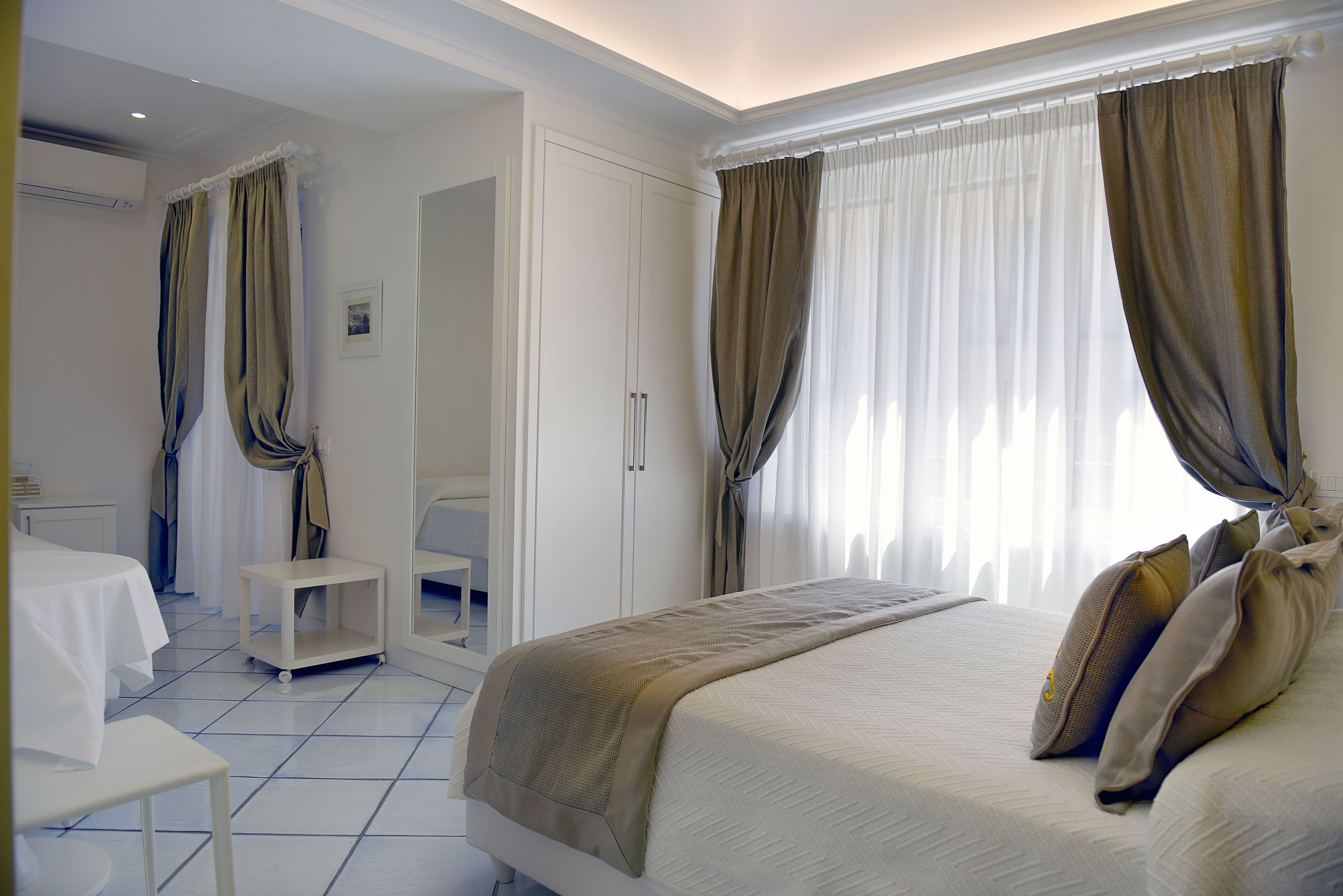 Una habitación de hotel con cama, una mesita, un armario y una ventana con cortinas.