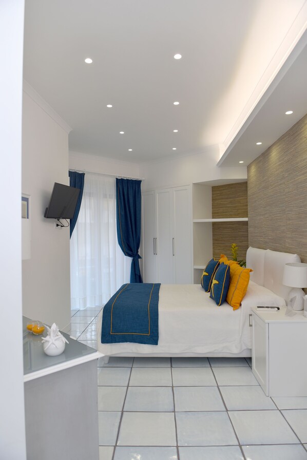 A modern hotel room with a neatly made bed, a flat-screen TV mounted on the wall, and a small bedside table with a lamp. - Maiori Luxury B&B (Maiori)