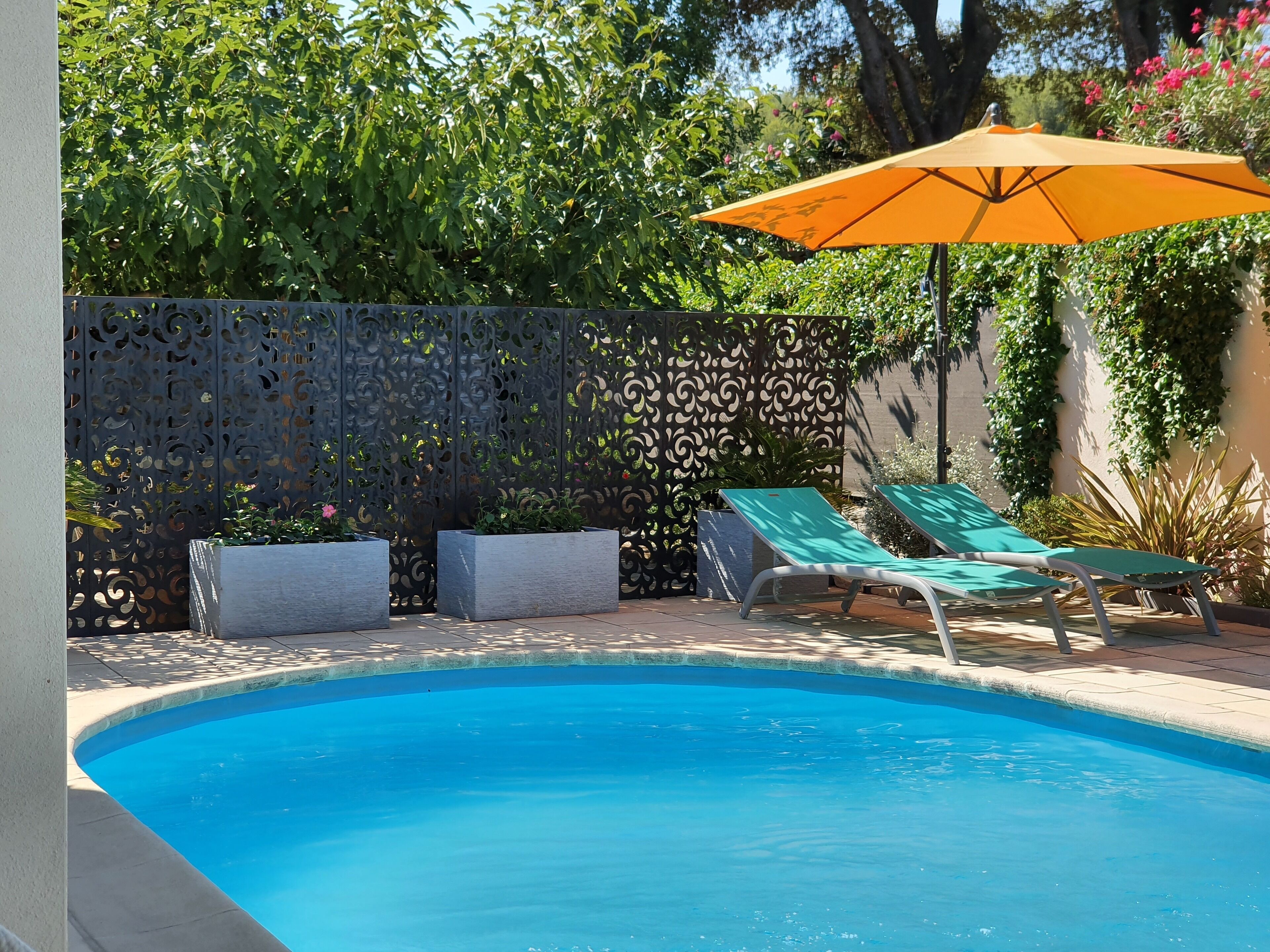 A swimming pool with two lounge chairs and an orange umbrella.
