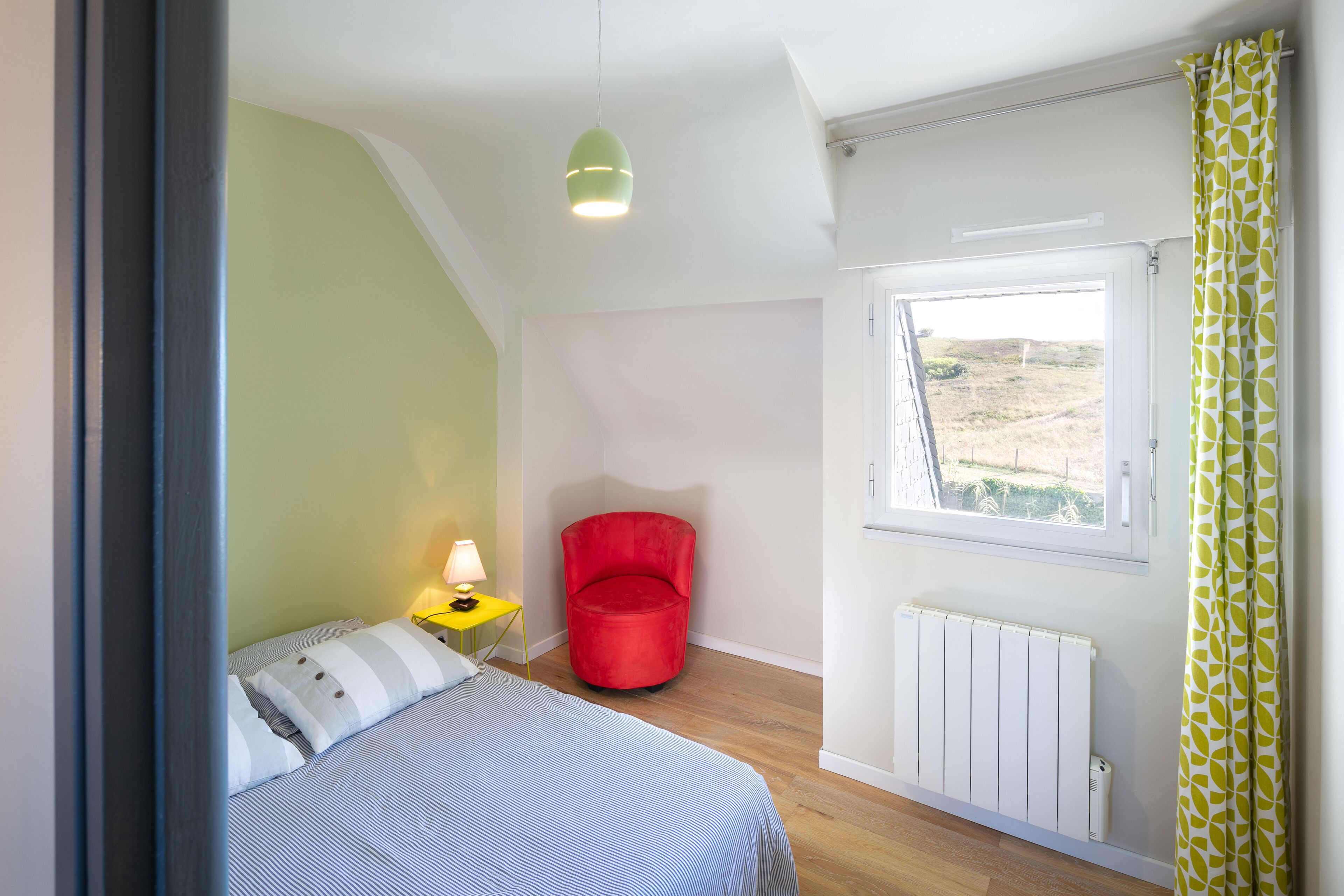 Un dormitorio con una cama, una silla roja, una ventana y un radiador.