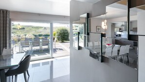 Un espace de repas moderne avec une cloison en verre, une cuisine dotée d’un grand miroir et une vue sur l’extérieur.