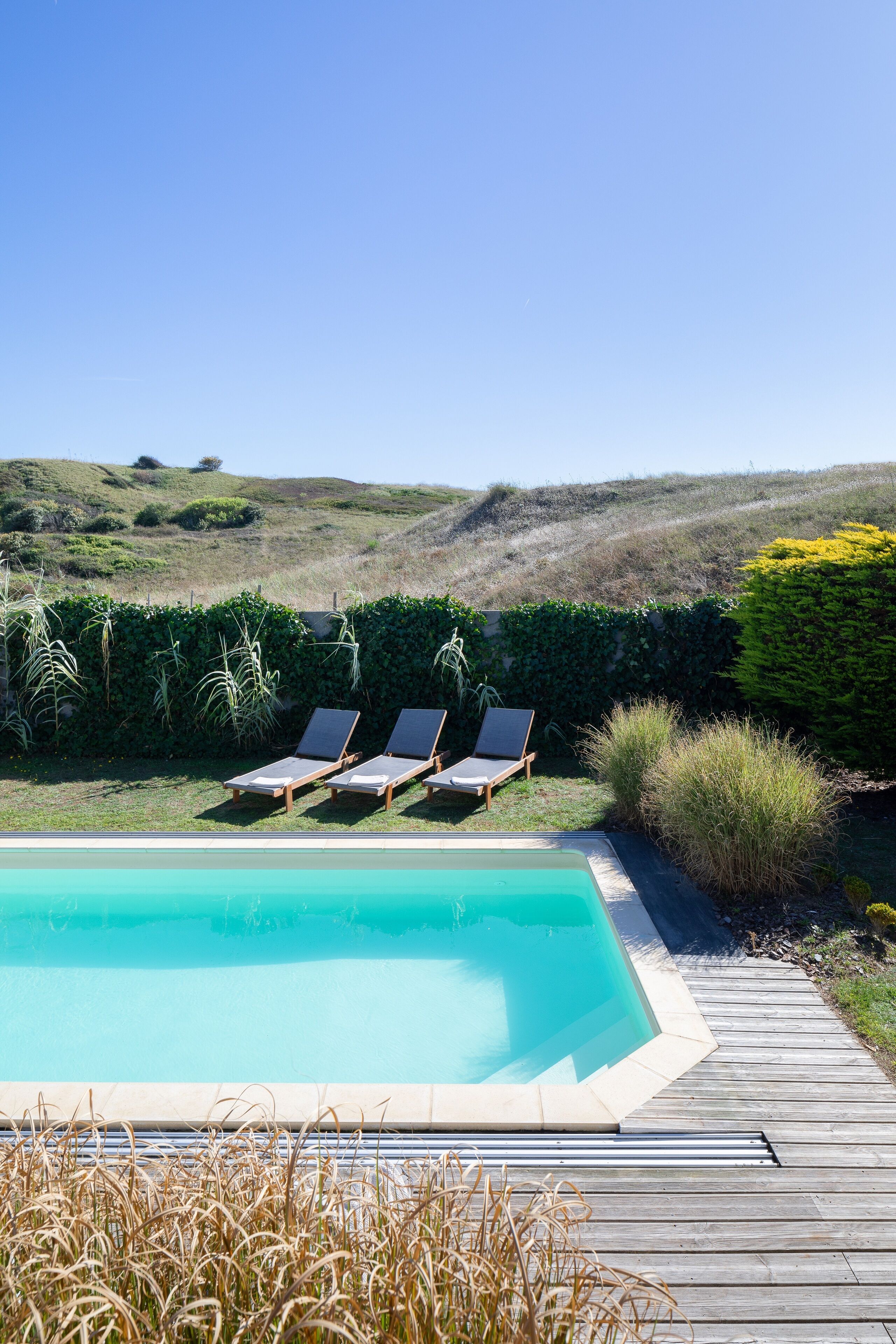 Una piscina con tre lettini prendisole e un pontile in legno.