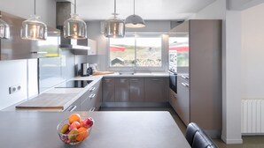 Une cuisine moderne dotée d’un grand îlot central, d’appareils électroménagers en acier inoxydable et de luminaires suspendus.