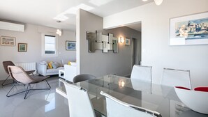 Un salon moderne avec une table à manger en verre, des canapés blancs et des fauteuils en osier.