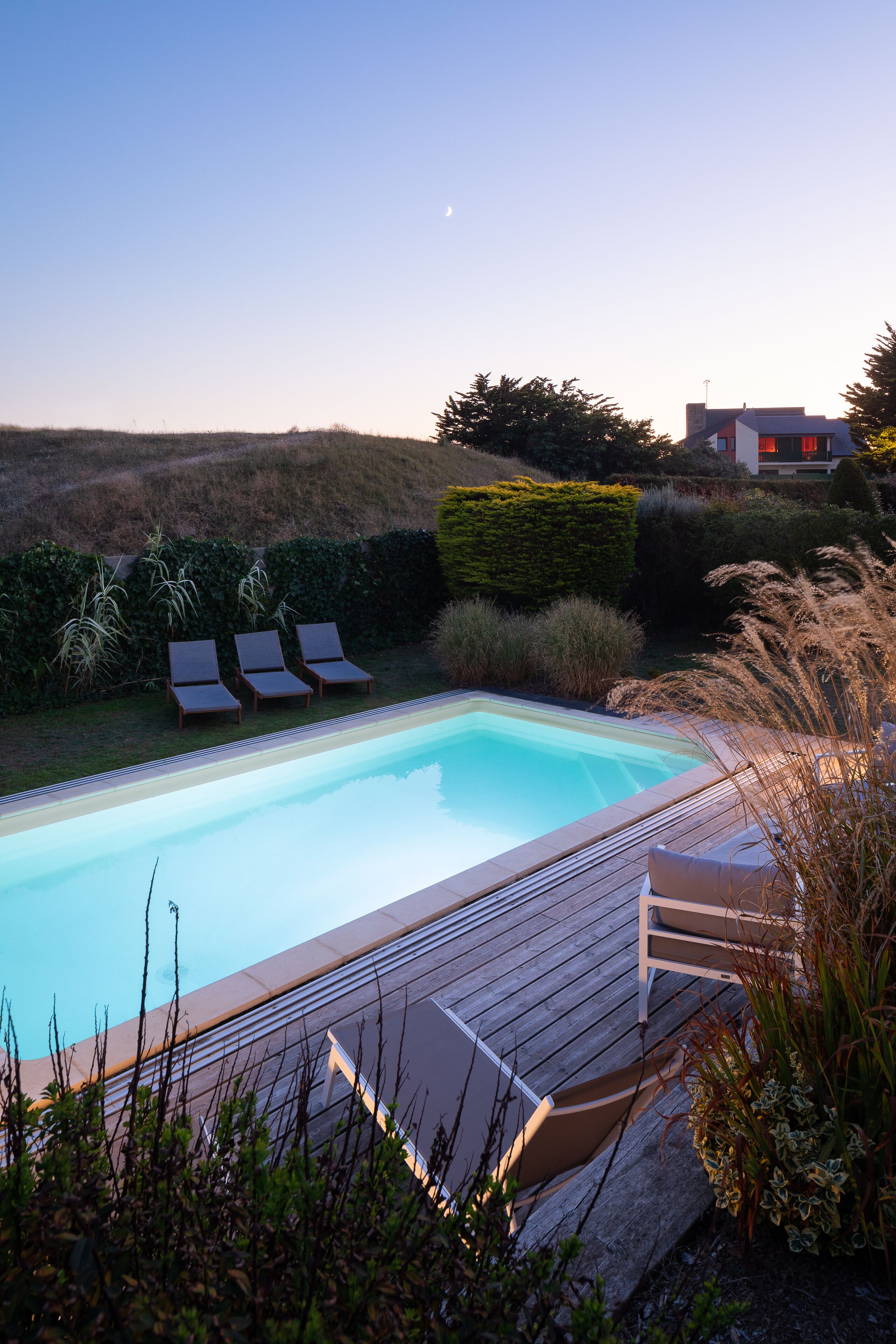 Una piscina rectangular amb terrassa de fusta i gandules.