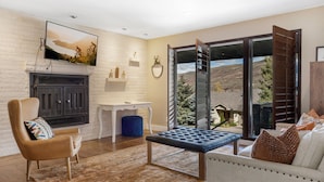 A living room with a fireplace, a sofa, a chair, a coffee table, and a view of a mountainous landscape through large sliding glass doors. - Vail mountain house! 5 bedrooms plus loft.  Hot tub! (Vail)