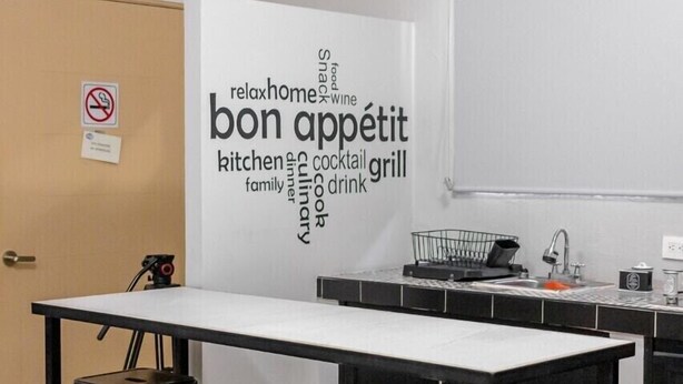 A kitchen area with a whiteboard displaying various food-related words, a long table with four stools, and a no-smoking sign on the door.