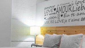 A bedroom with a bed, a nightstand, a lamp, and a wall with love-themed text.