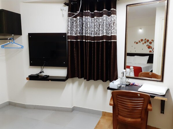 Habitación de hotel con televisor de pantalla plana en la pared, un escritorio con silla, un espejo y una cama con decoración floral.