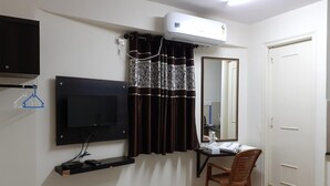 Une pièce équipée d’un téléviseur fixé au mur, d’un appareil de climatisation, d’un bureau avec une chaise, d’un miroir et d’une porte.