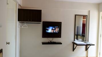 A hotel room with a television mounted on the wall, a mirror above a small table, and a door to the left.