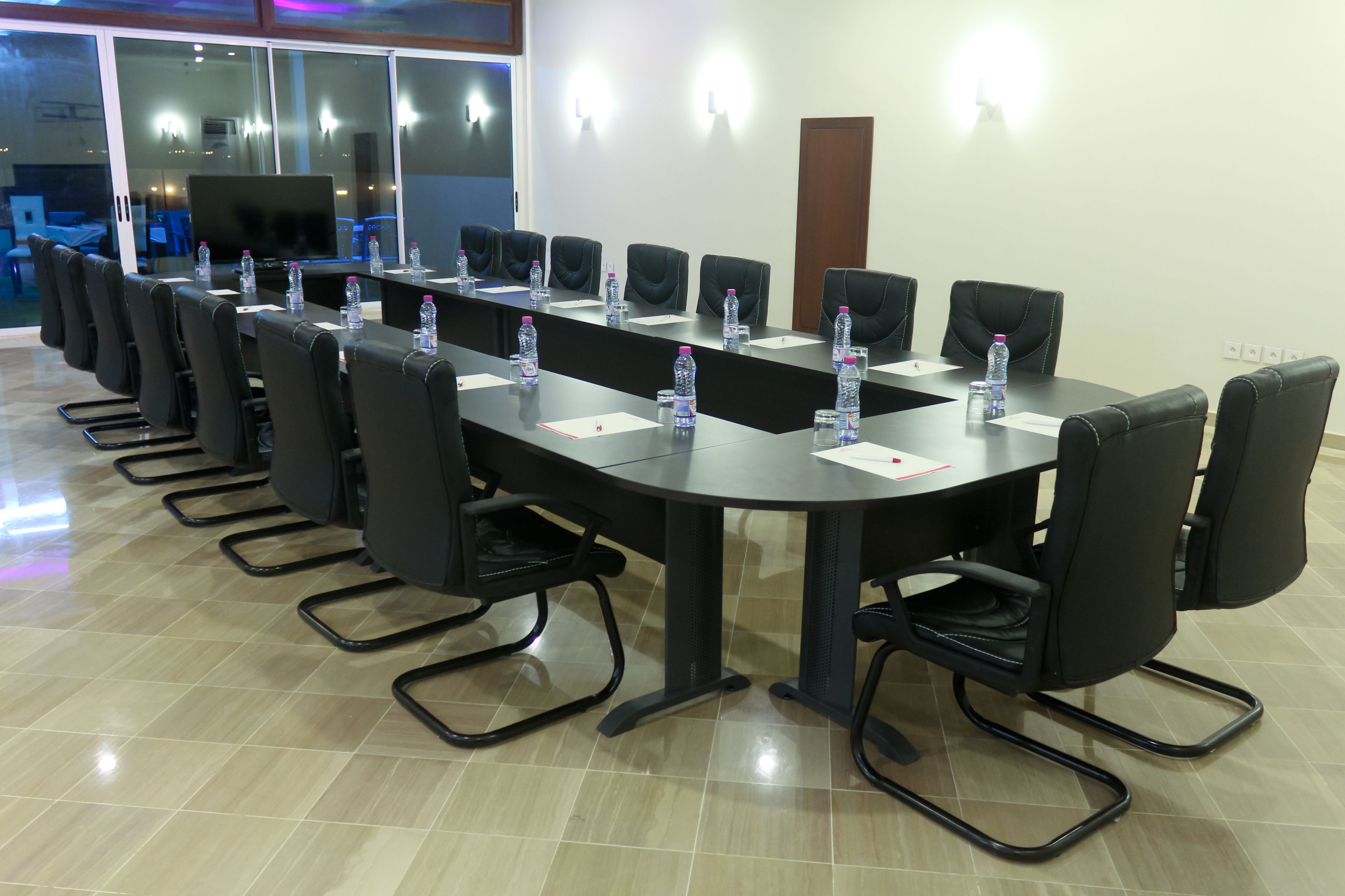 A conference room with a long table, black chairs, water bottles, and a flat-screen TV.