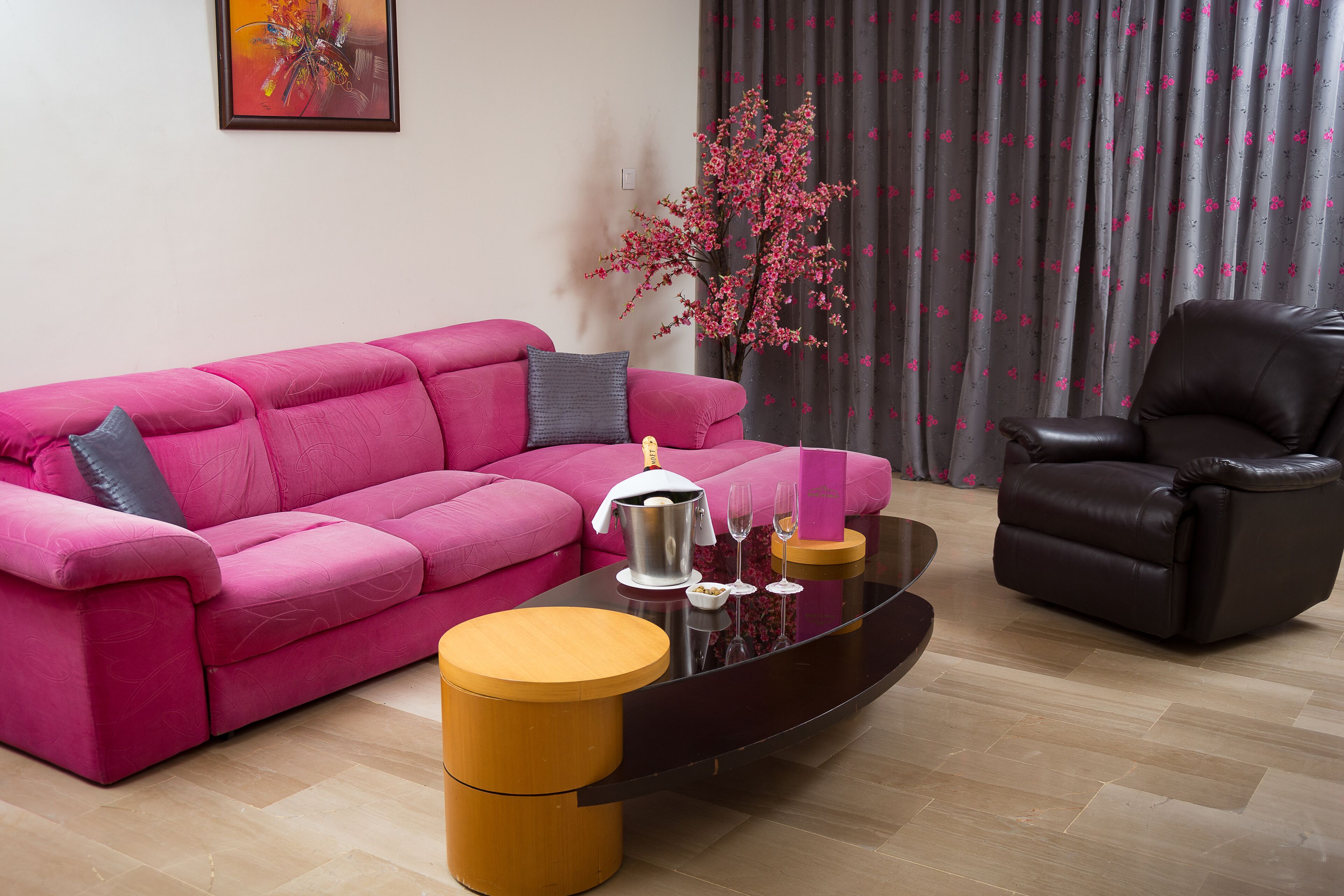 A modern living room with a pink sofa, a brown leather chair, a glass coffee table, and a decorative plant.