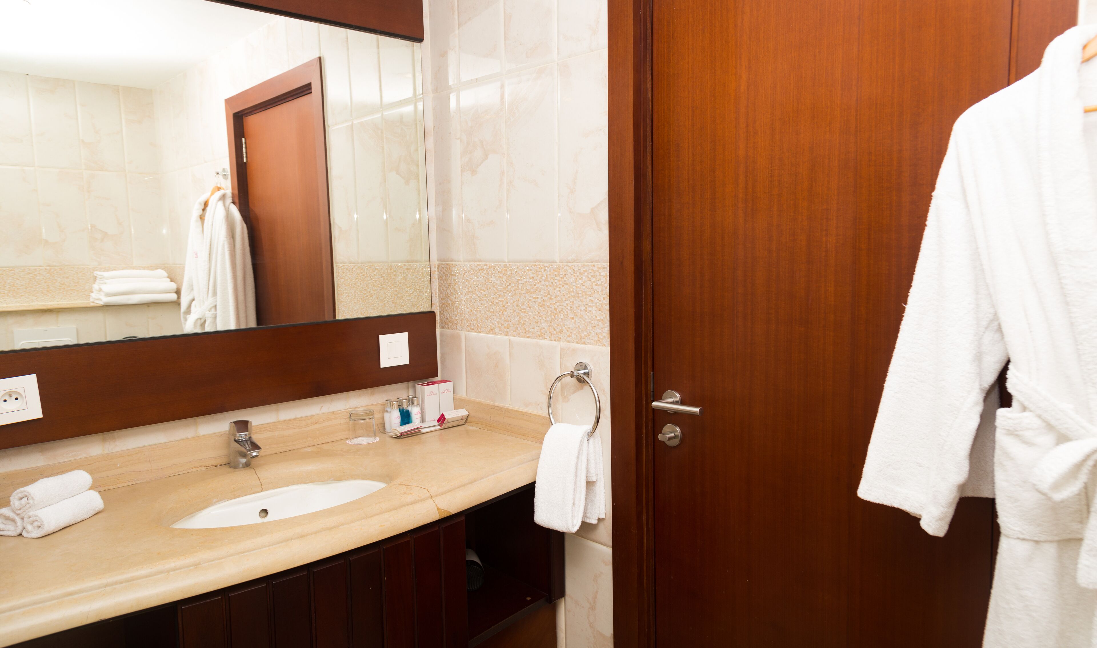 A hotel bathroom with a wooden door, a large mirror, a sink, and a towel rack.