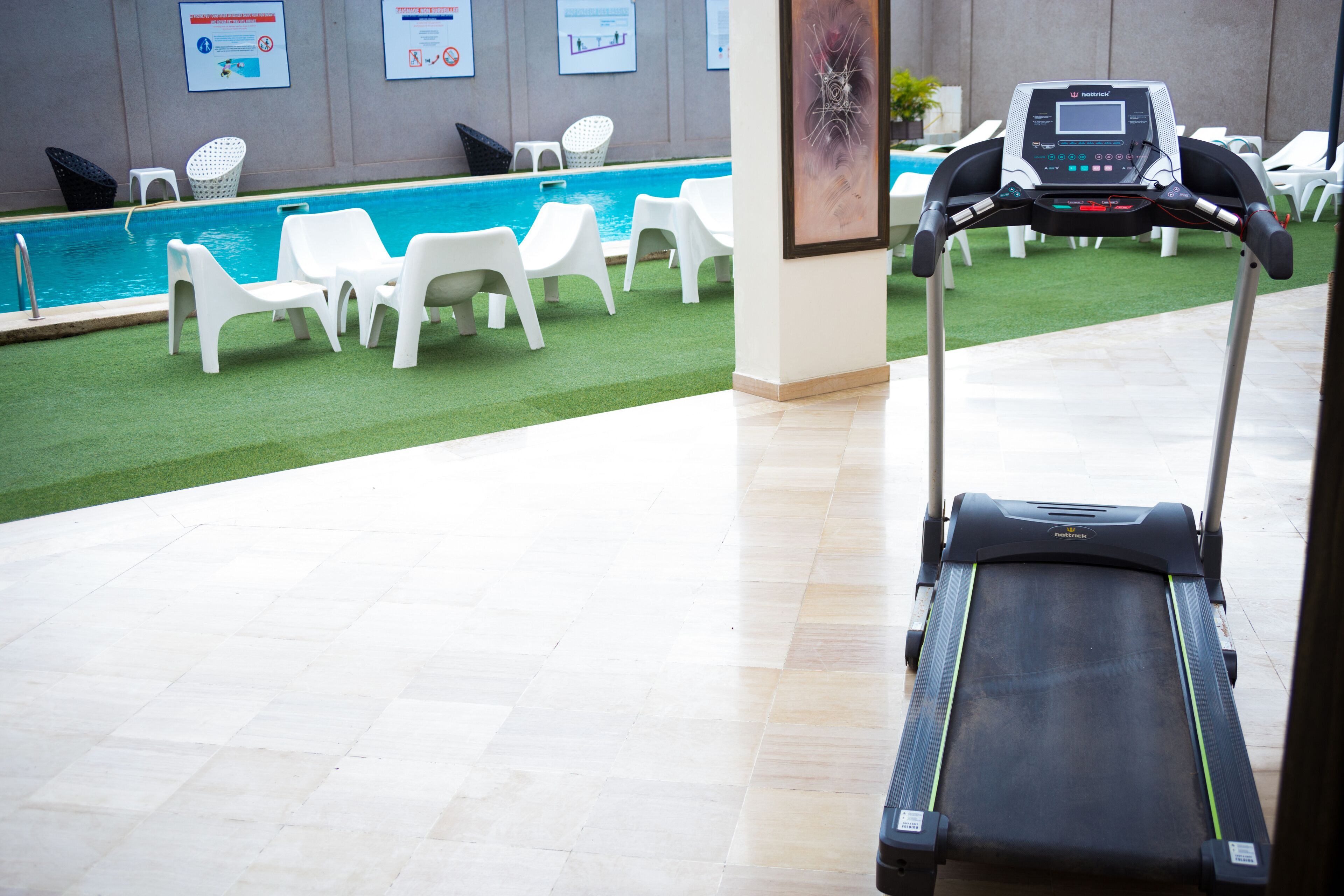 Esteira numa área de lobby de hotel, com piscina e cadeiras de descanso ao fundo.