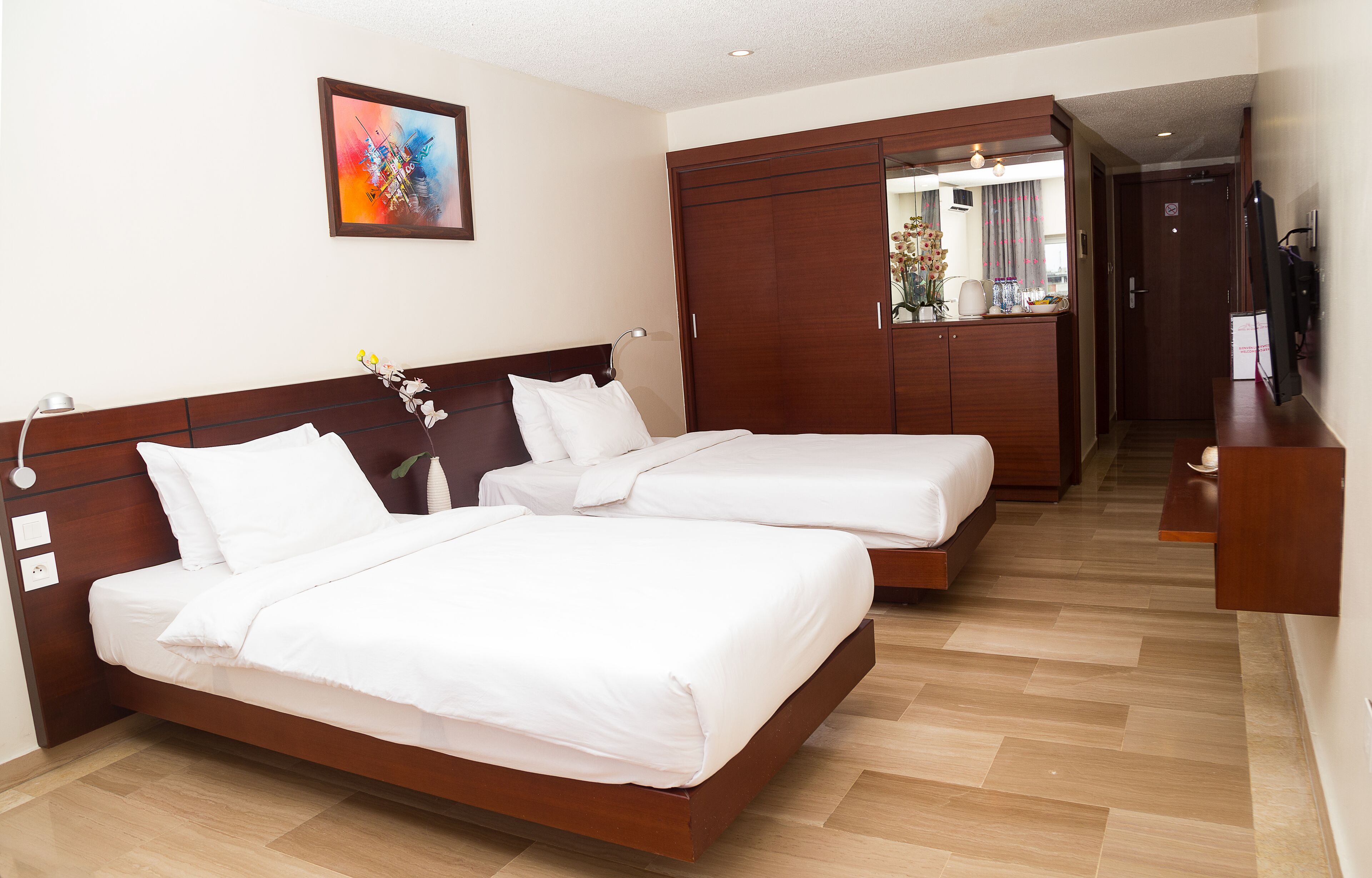 A hotel room with two beds, wooden headboards, a large mirror, and a wooden wardrobe.