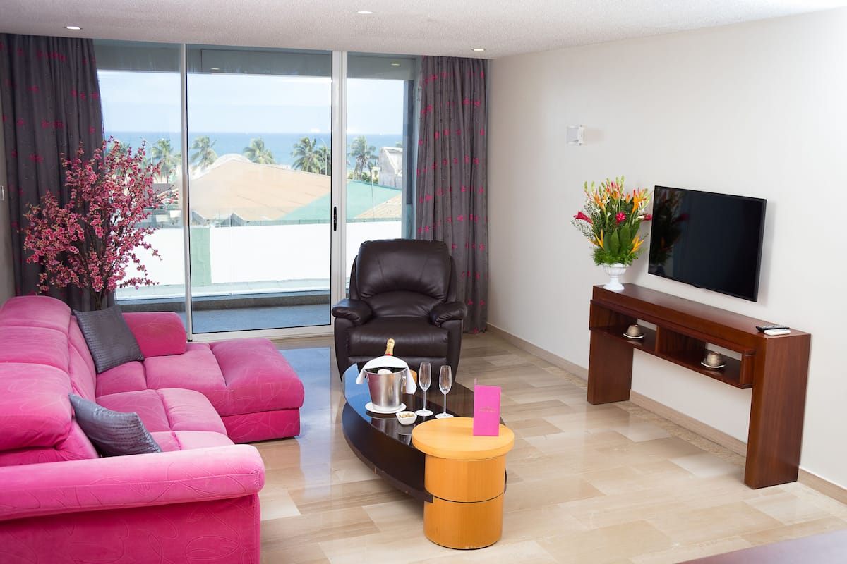 A modern living room with a pink sofa, a black leather chair, a wooden coffee table, and a TV on a wooden stand.