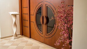 A wooden wardrobe with a glass door, a pedestal table, and a vase with pink flowers. - Hôtel du Golfe (Lomé)