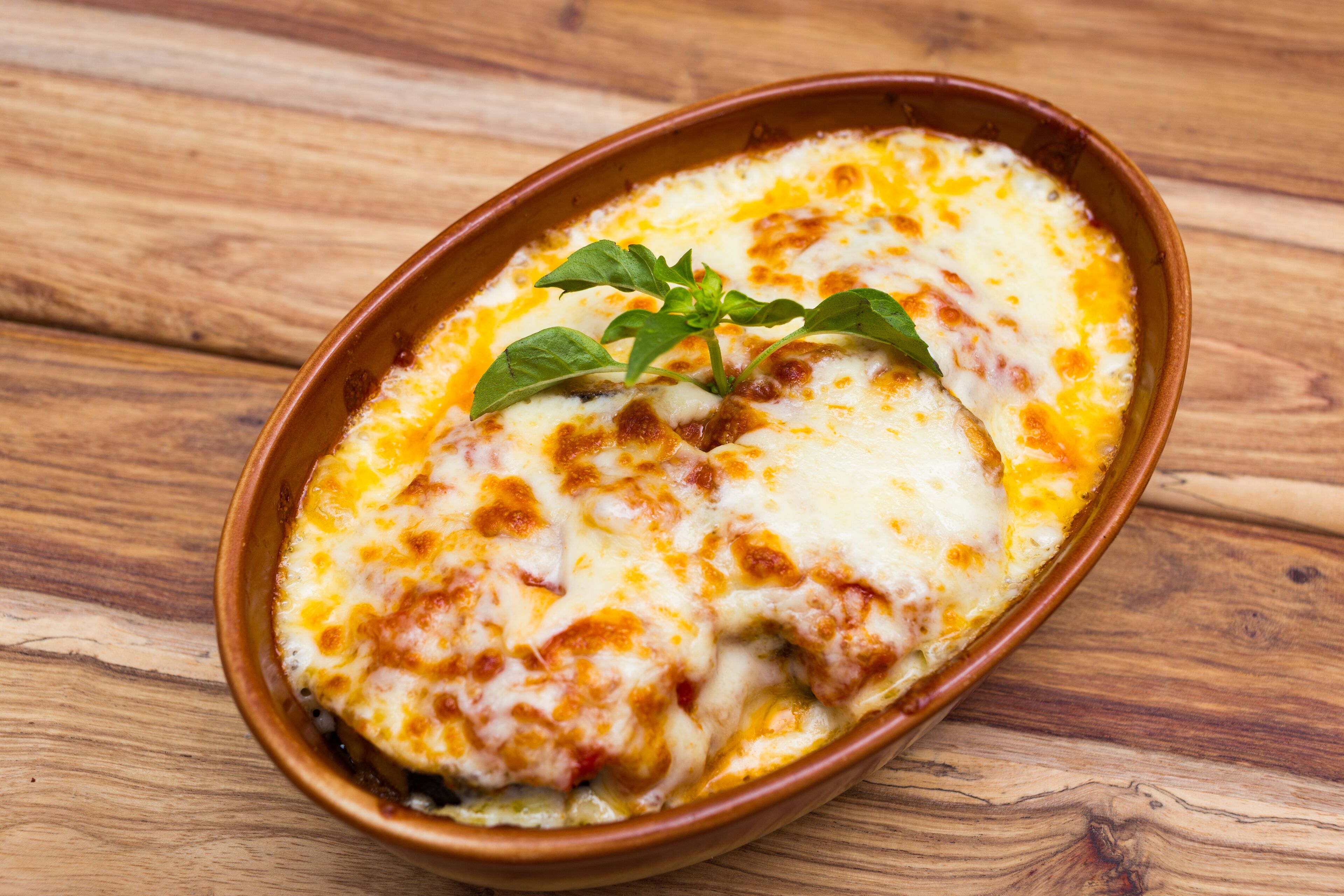 Un plato de cerámica con queso gratinado, decorado con una hierba verde, sobre una superficie de madera.