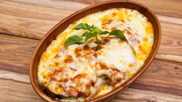 Un plato de cerámica con queso gratinado, decorado con una hierba verde, sobre una superficie de madera.