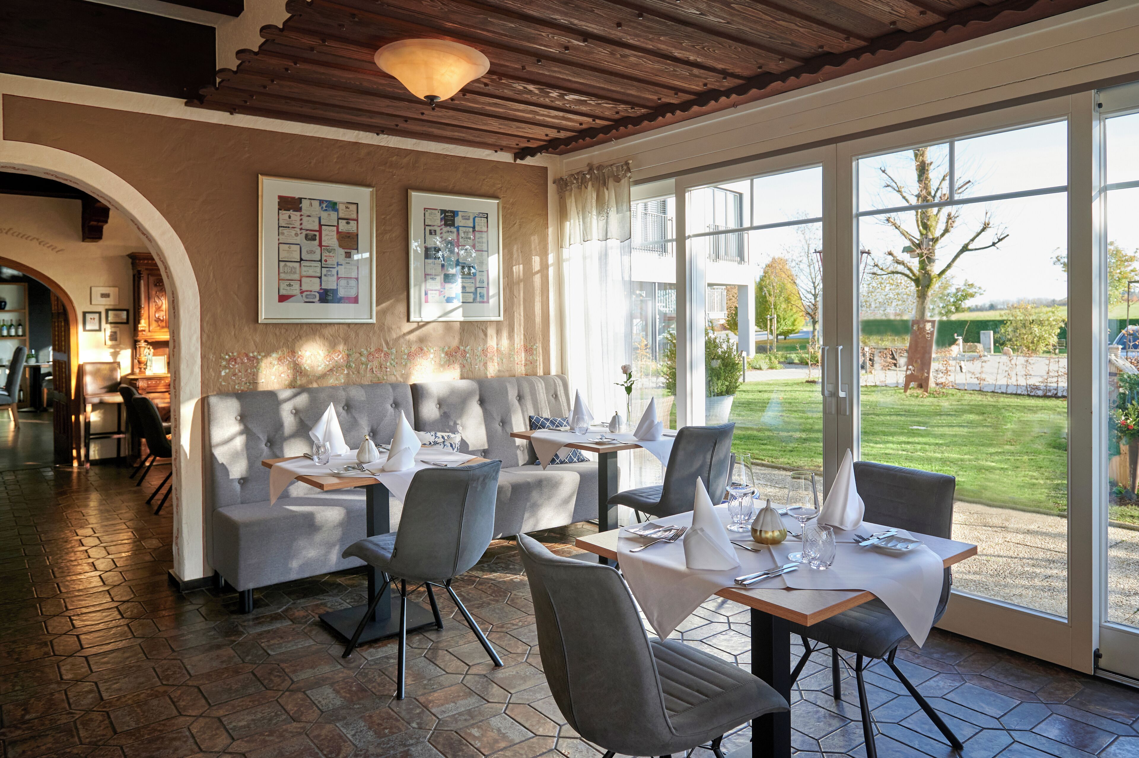 A restaurant with a patio area, tables with white tablecloths, and a view of the garden.