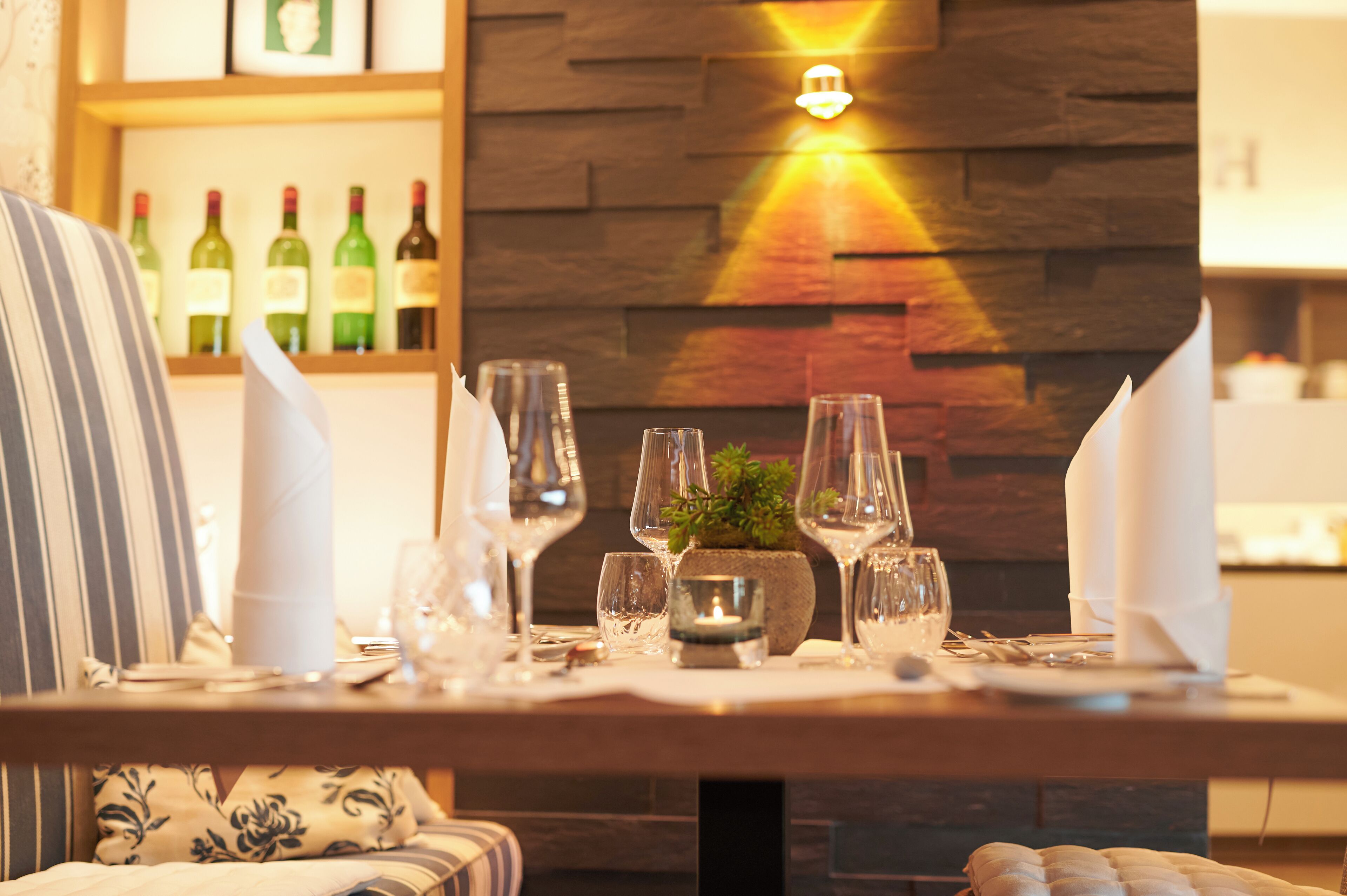 Una mesa de comedor dispuesta con copas de vino, una vela y un pequeño centro de mesa con planta.